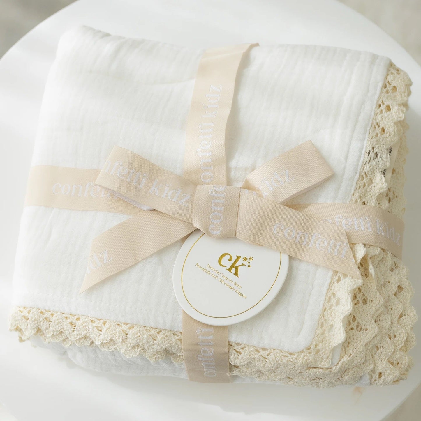 White lace baby blanket with a ribbon and 'CK' logo on a white surface