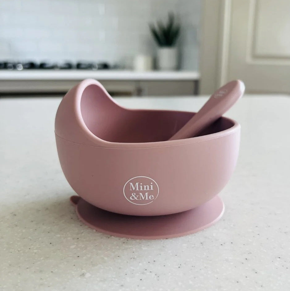 Pink bowl with suction cup and spoon on a kitchen counter, featuring 'Mini & Me' branding.
