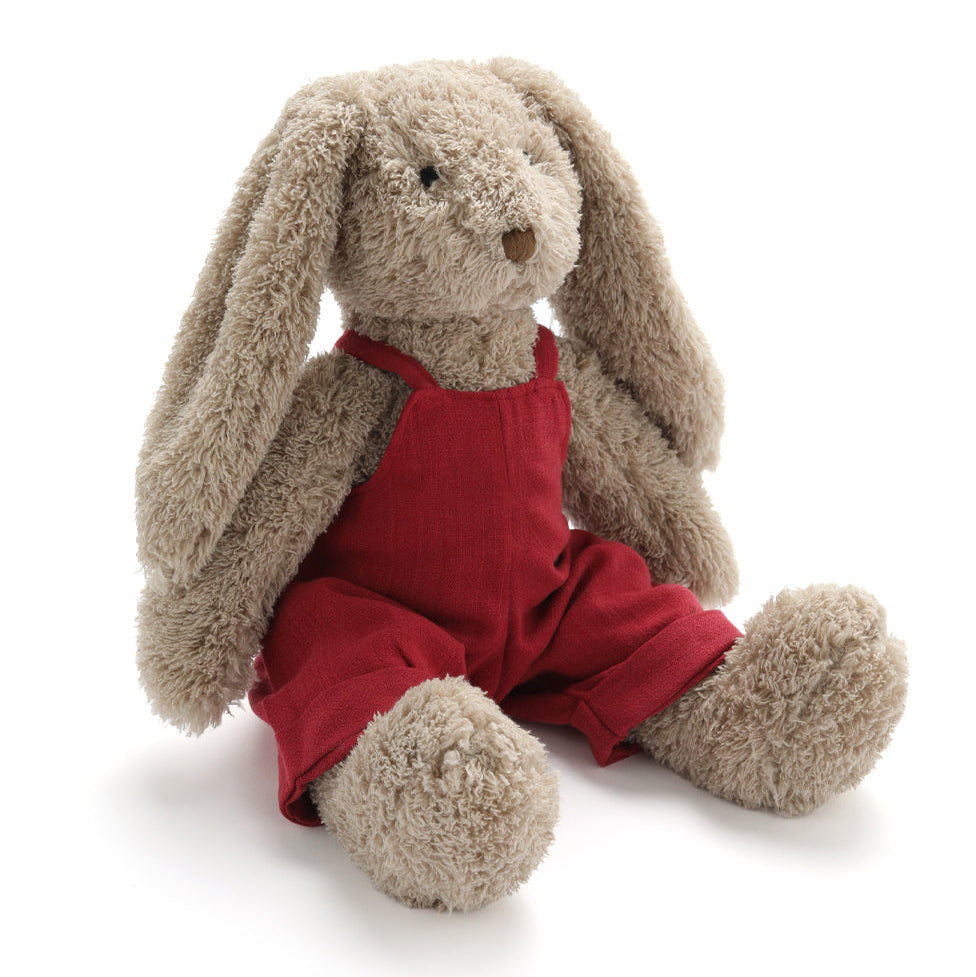 Stuffed bunny toy wearing red overalls on a white background