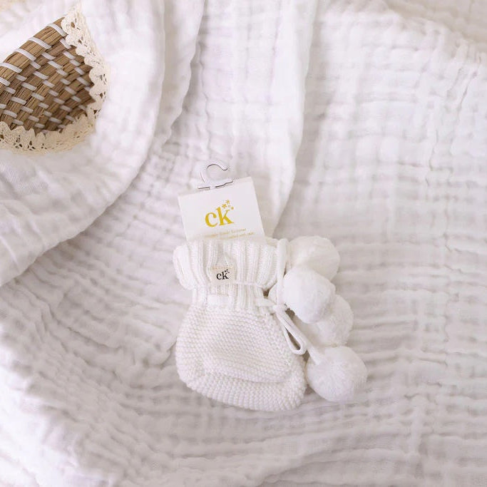 White textured blanket with a small basket and white socks on top, featuring the brand 'CK'.