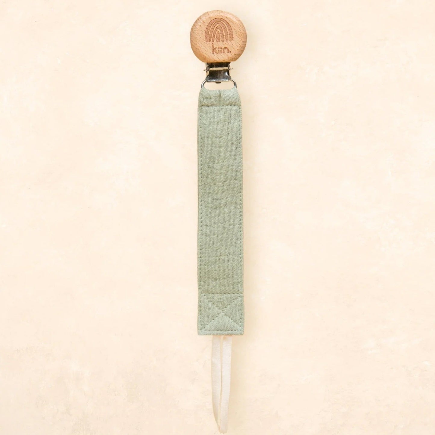 A single product shown against a plain textured beige background. The product is a long, narrow tool with a round light wood top, a pale sage green wrapped handle, and a clear pointed tip extending from the bottom.