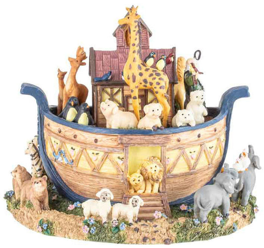 A Noah's Ark figurine featuring a detailed wooden ark with blue trim, filled with animal figures including a giraffe, lions, bears, sheep, penguins, and birds, set on a grassy base with additional animals around it.