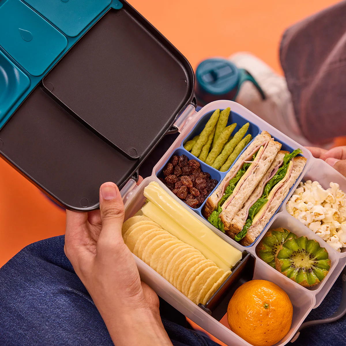 Person holding a compartmentalized lunch box with various food items on an orange background