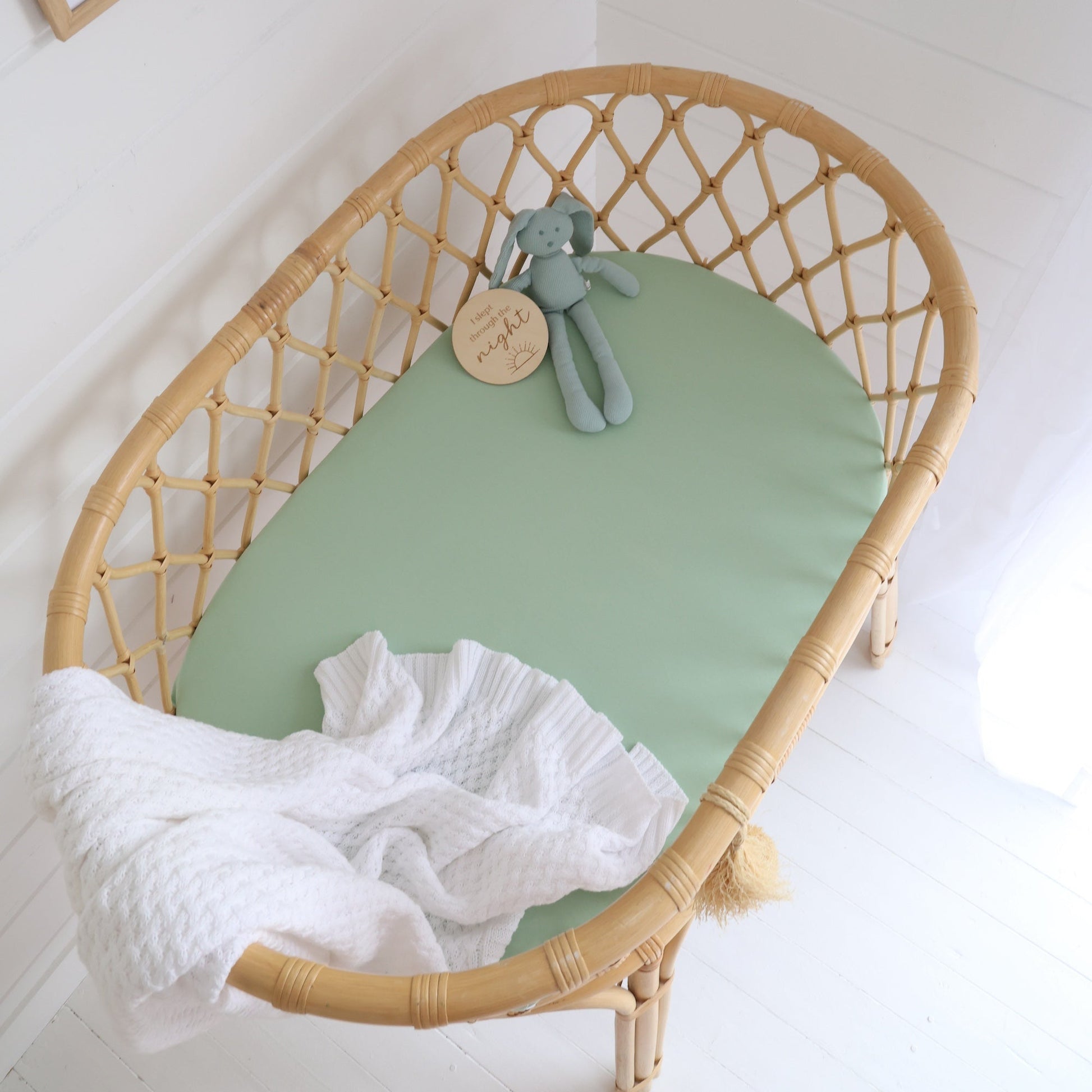 Wicker crib with green mattress and white blanket in a child's room.