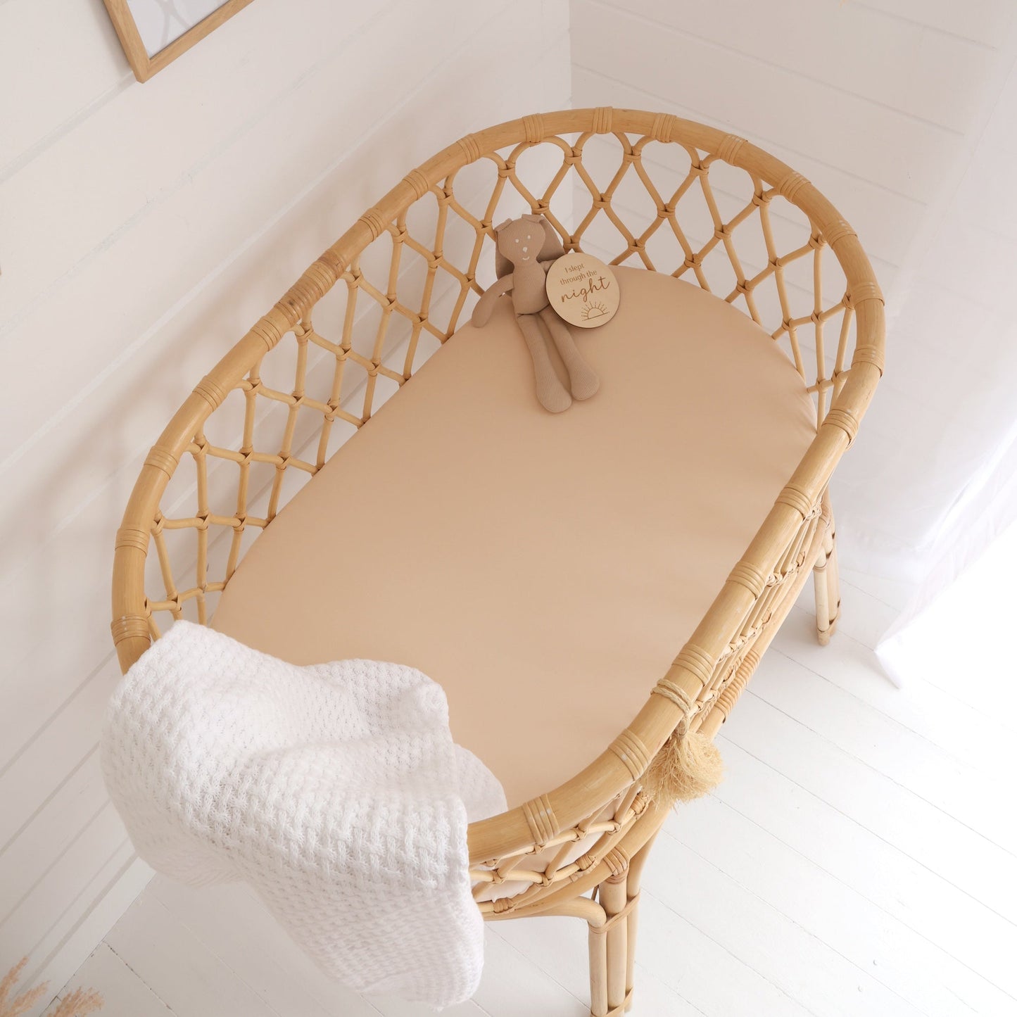 Wicker crib with beige mattress and white blanket in a nursery setting.