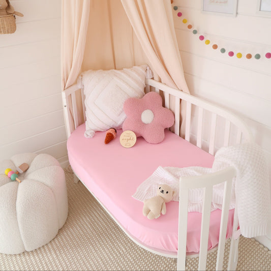 Children's room with a canopy over a crib, pink mattress, and decorative pillows.