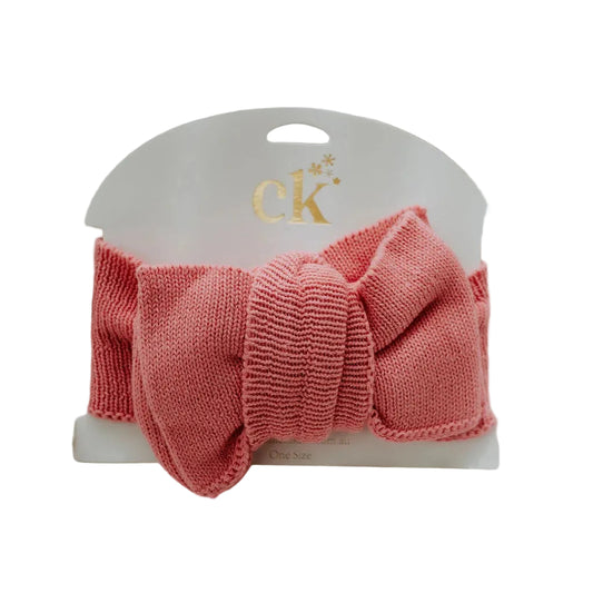 Pink knitted headband on a white card with a brand logo, placed on a textured surface.
