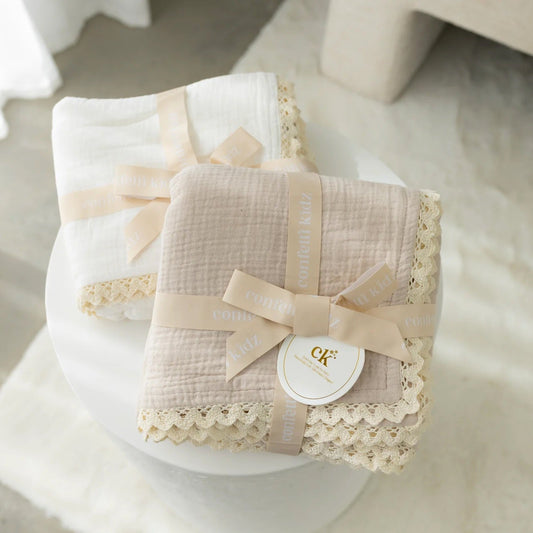 Baby blanket with lace trim and bow on a white surface