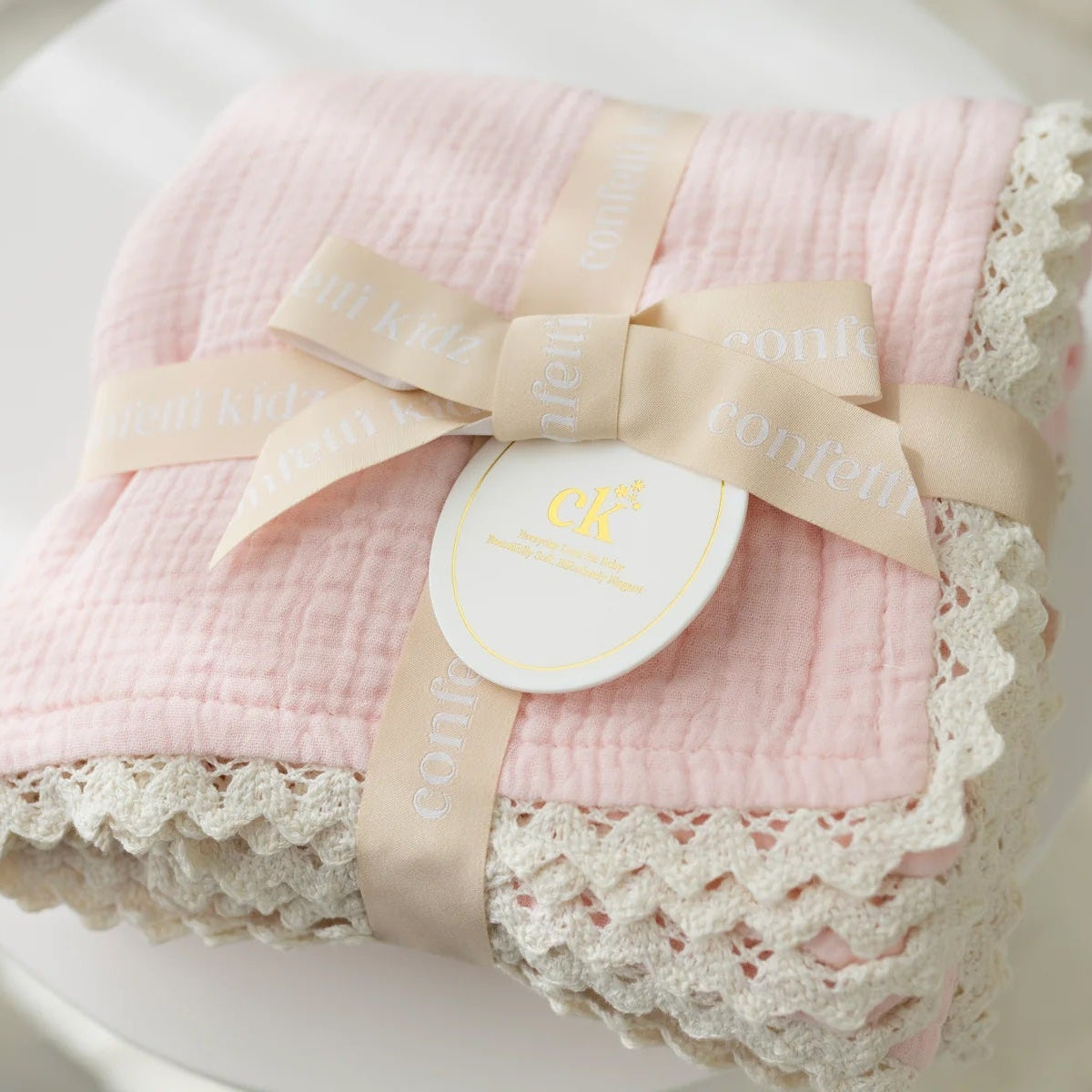 Pink baby blanket with lace edges and a bow on a white surface