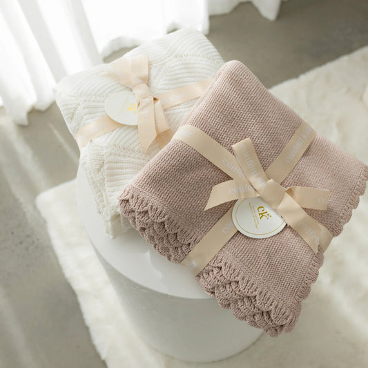Two baby blankets with ribbons on a white surface