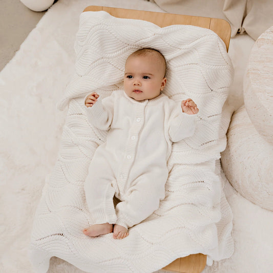Baby wrapped in a white swaddle blanket on a wooden surface