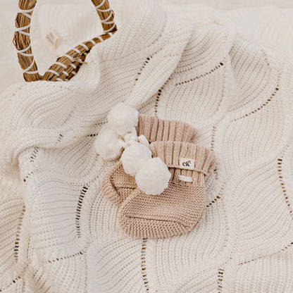 Knitted baby bootie with pom-pom on a textured blanket