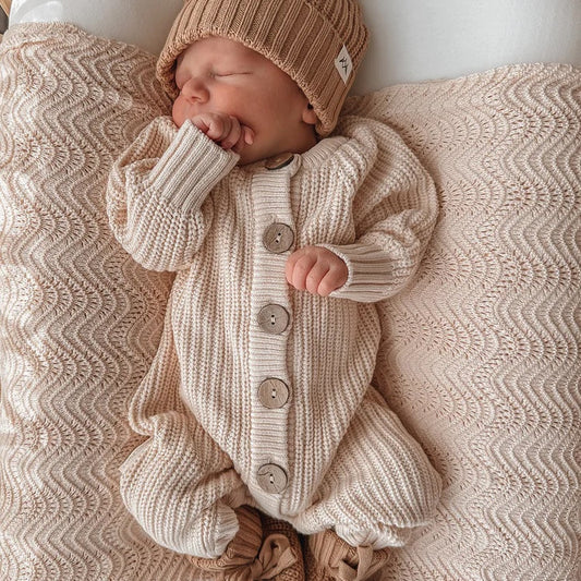Newborn baby in a knitted outfit and hat lying on a textured blanket.