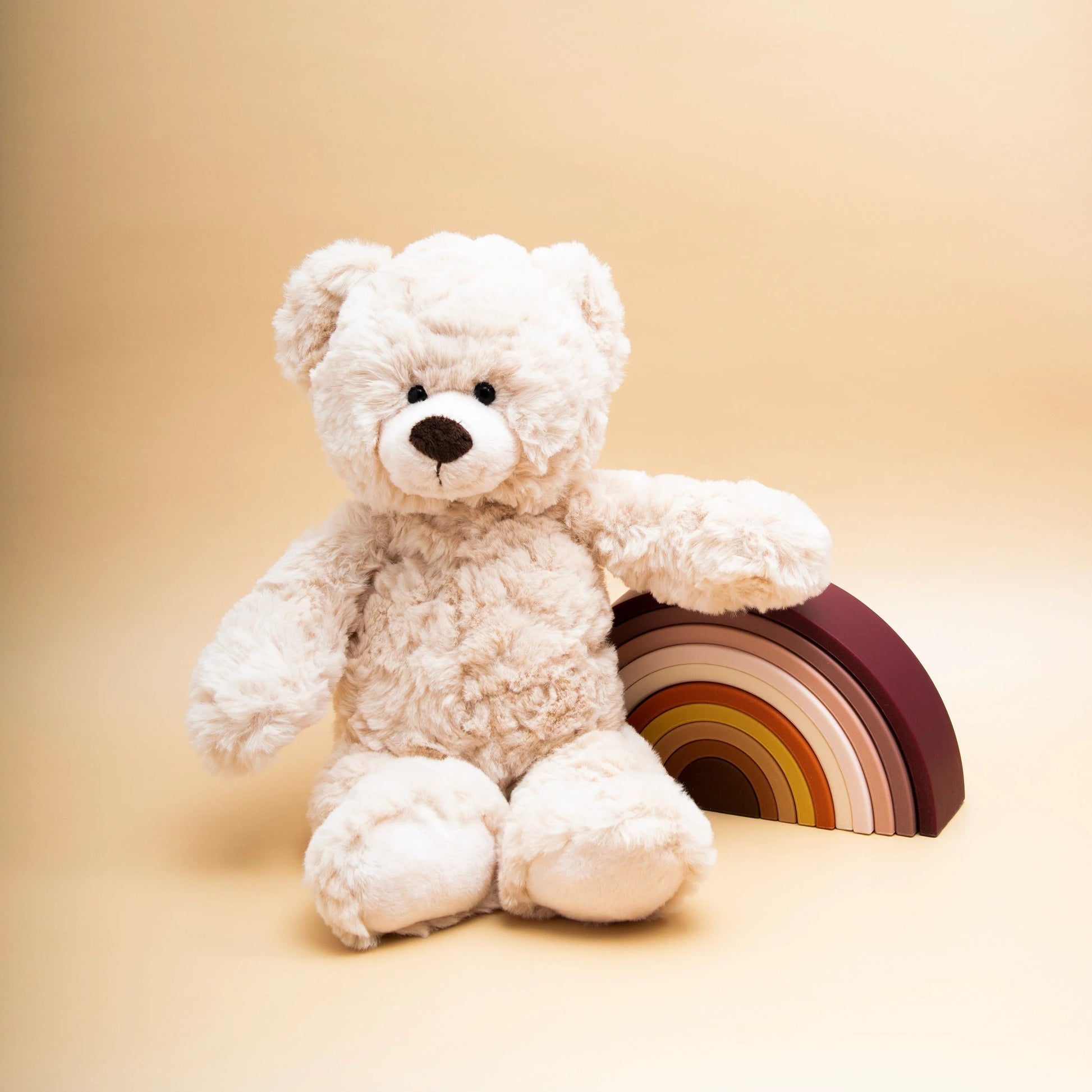 White teddy bear holding a rainbow toy on a beige background