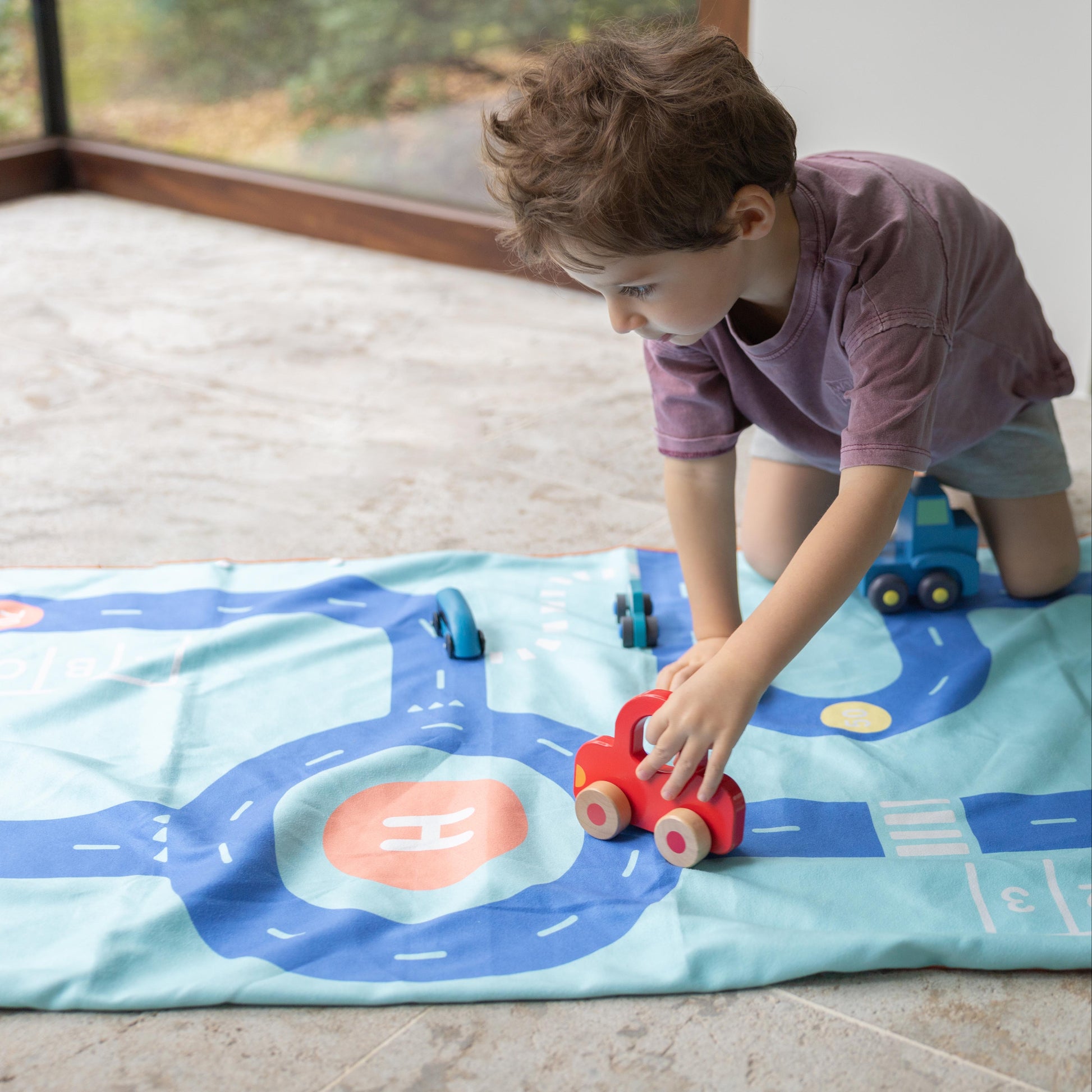 Child playing with toy cars on a road-themed play mat