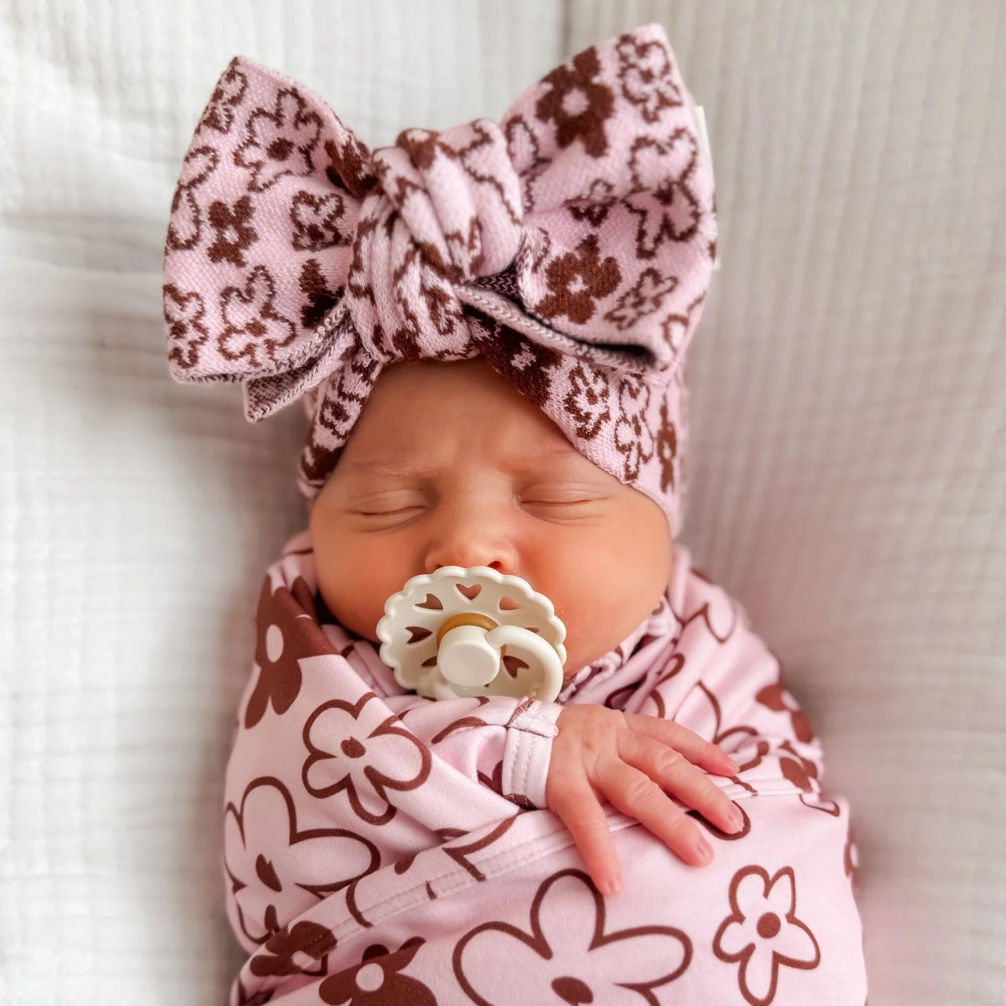 Newborn baby swaddled in a pink and brown floral pattern with a matching headband.