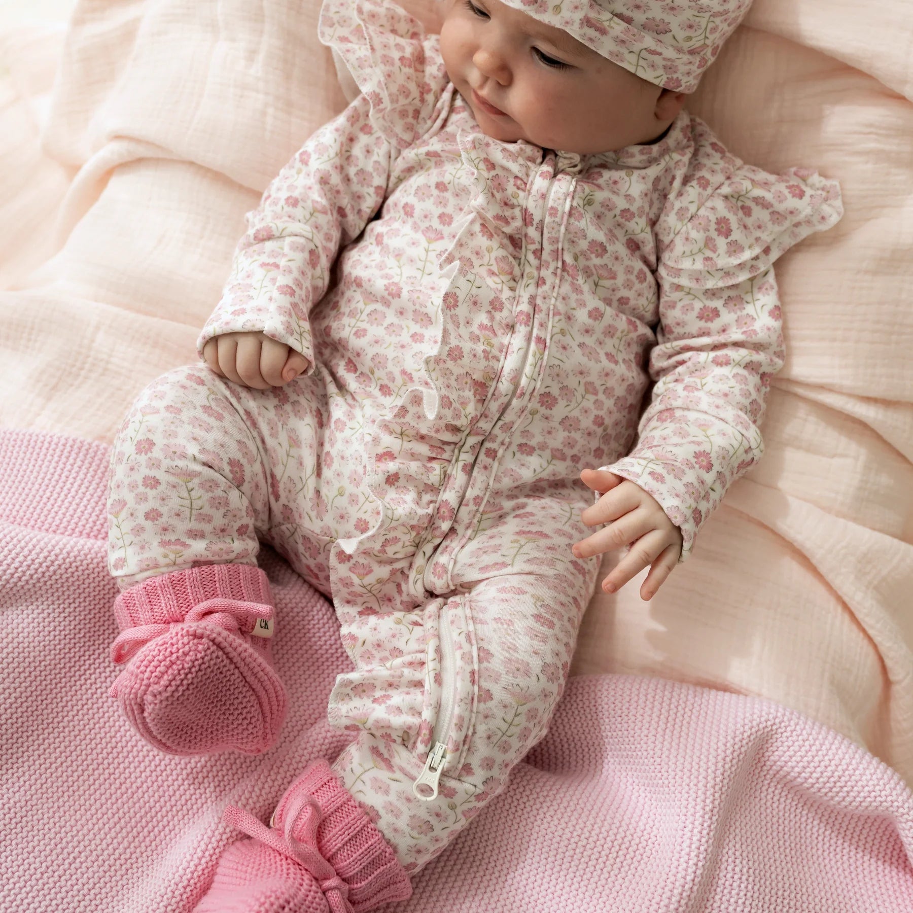 Baby in a floral outfit with a large bow on a pink blanket