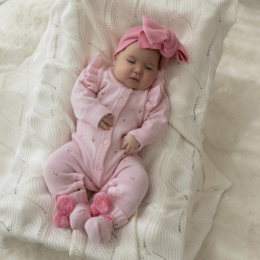 Baby in pink outfit and headband lying on a textured blanket
