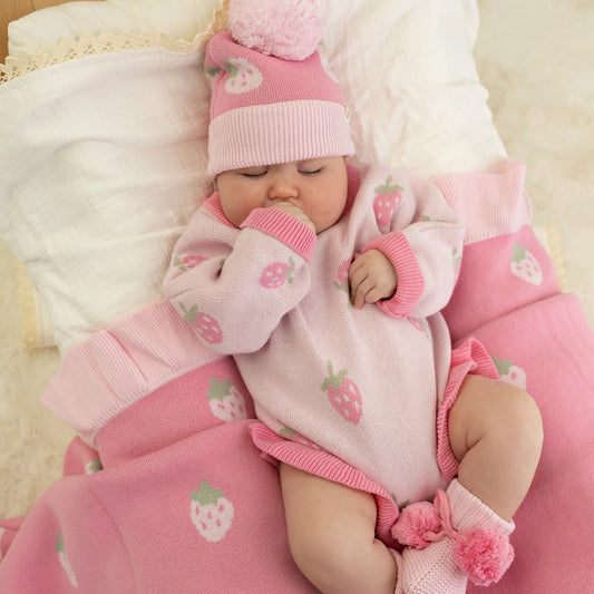 Baby in pink outfit with floral patterns lying on a pink cushion.