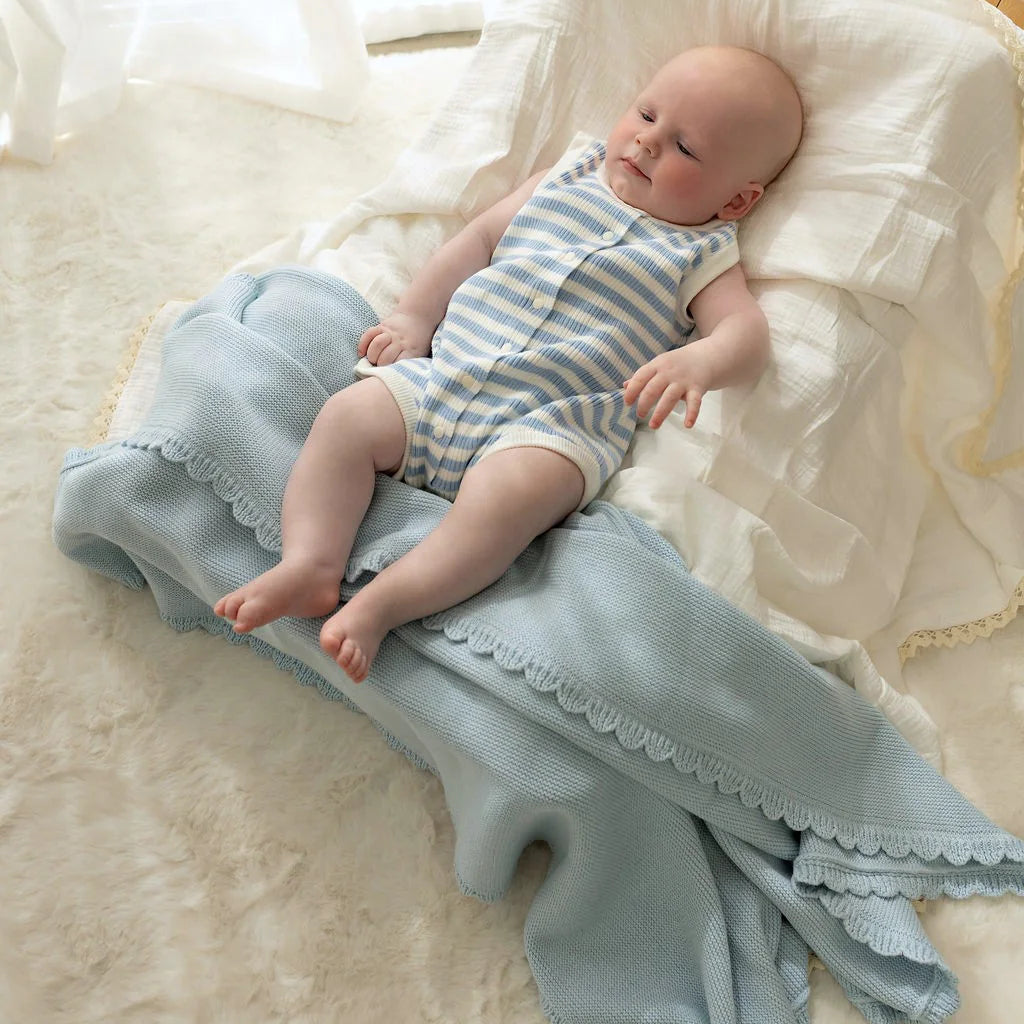 Newborn baby lying on a textured blanket with a soft white background