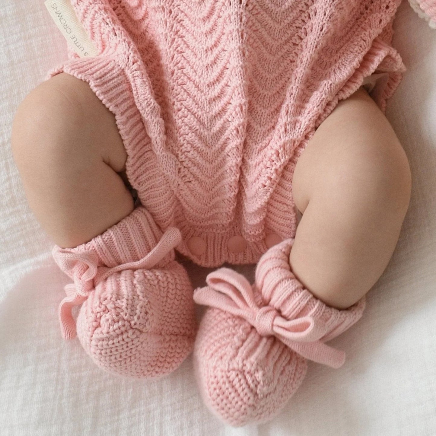 Baby wearing pink knitted outfit with matching booties on a soft white background