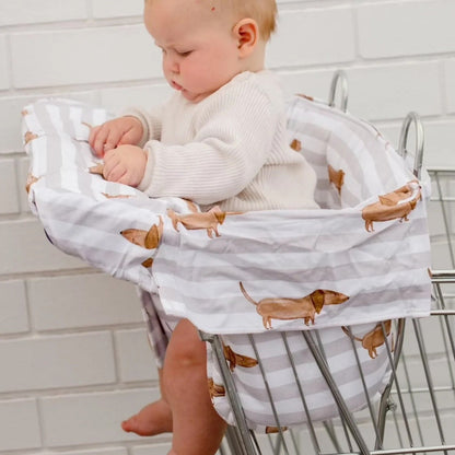 Baby in a shopping cart with a patterned cover featuring small dogs.