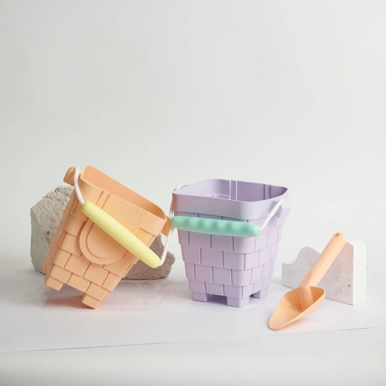 Two woven buckets, one peach and one purple, with a yellow handle and scoop on a light gray background.