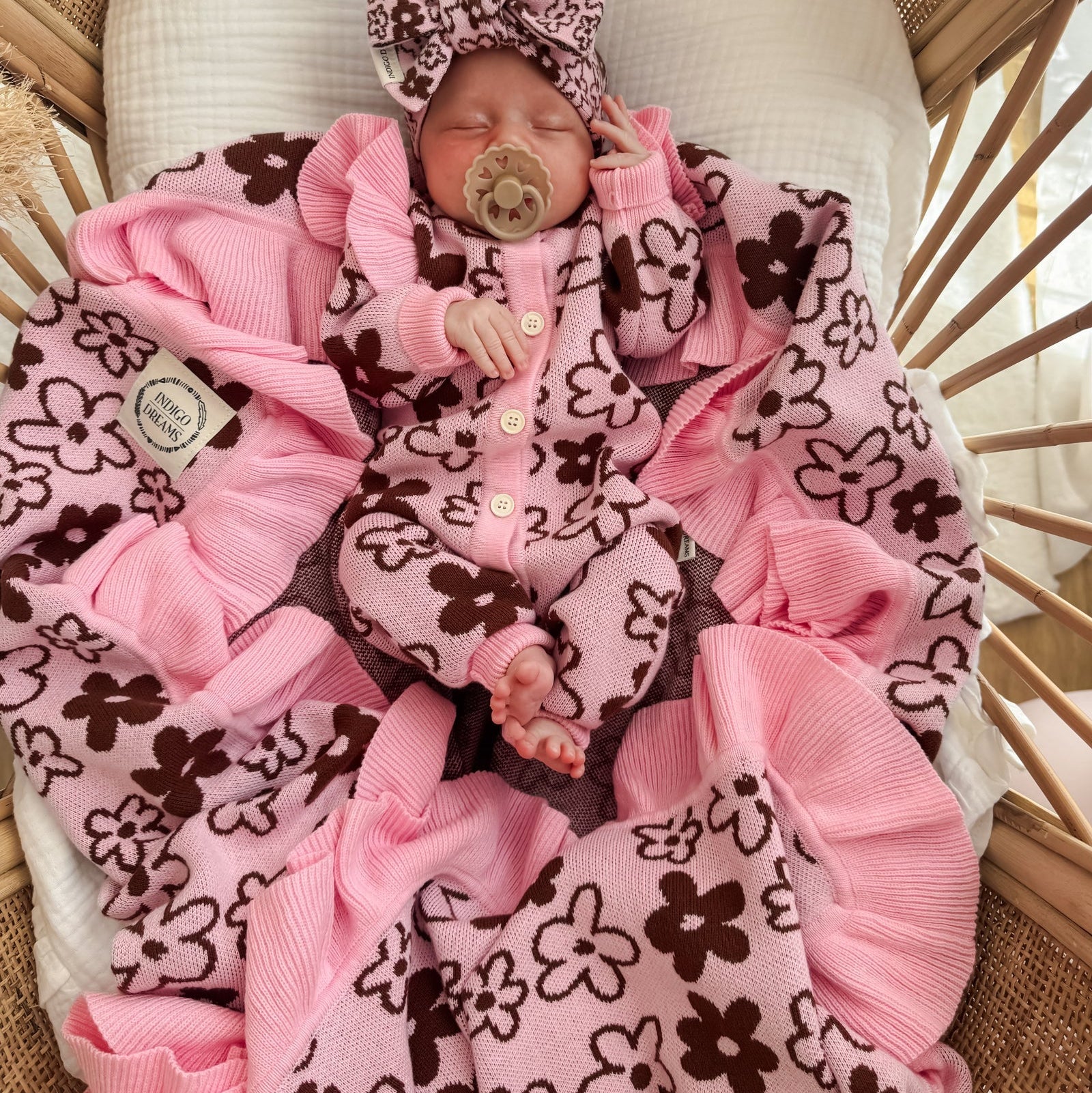 Newborn baby in a pink and brown outfit with a pacifier, lying on a textured blanket.