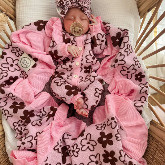 Newborn baby in a pink and brown outfit with a pacifier, lying on a textured blanket.