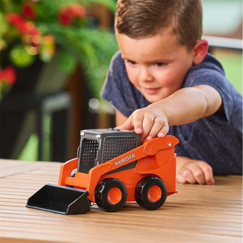 Child playing with a toy Kubota bulldozer on a wooden surface.