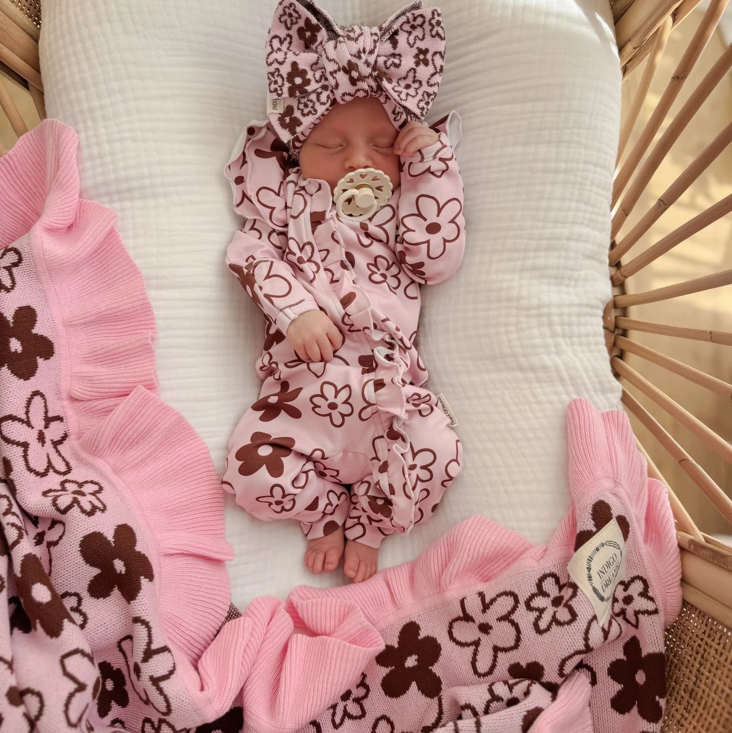 Newborn baby in a floral outfit with matching headband and blanket in a crib.