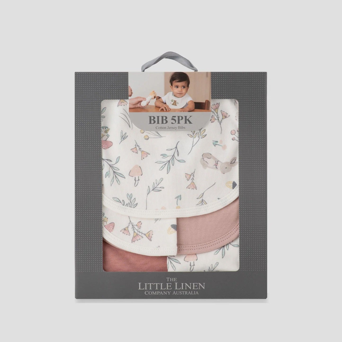 Packaged baby bibs with floral and pink designs in a gray box, featuring 'The Little Linen Company' branding.