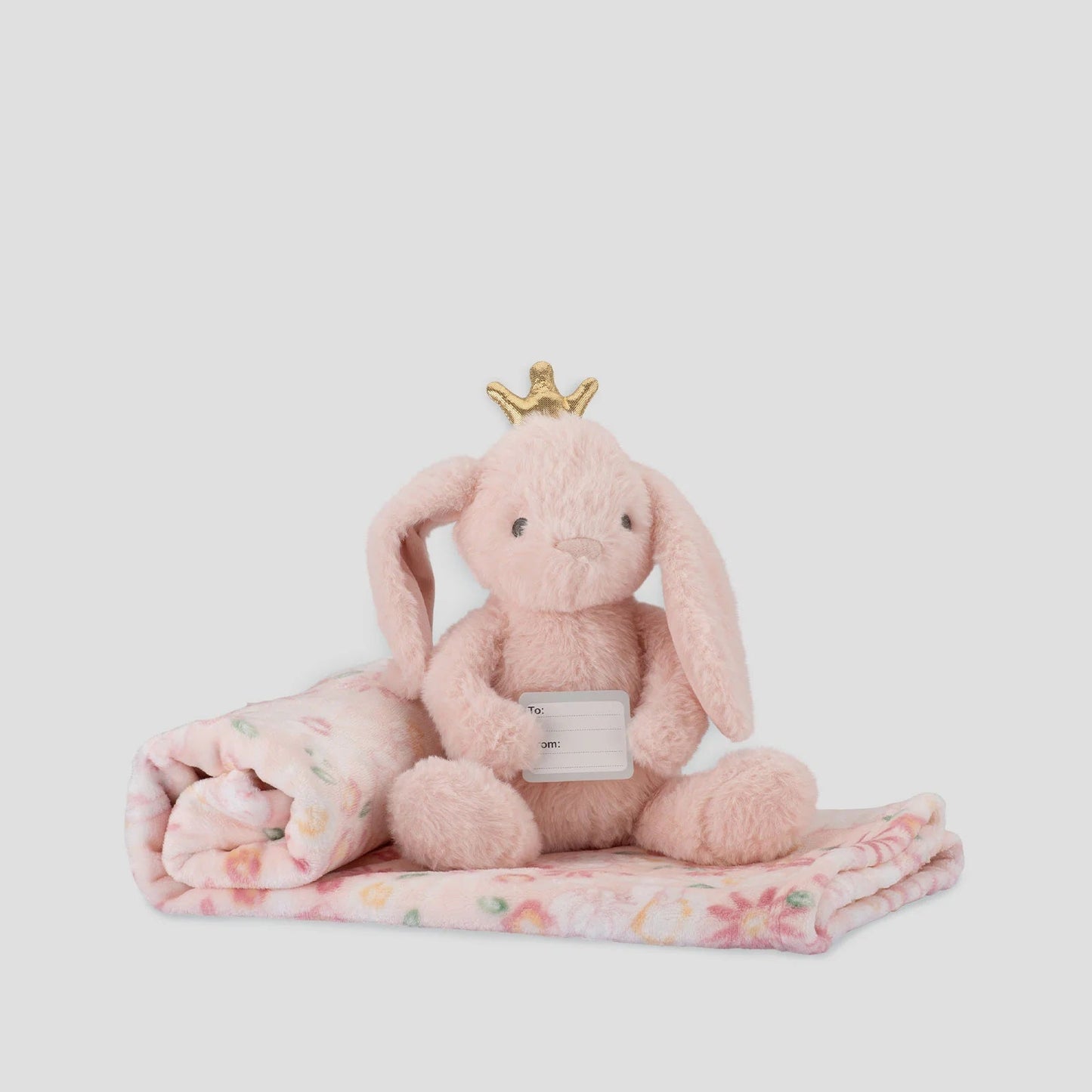 Pink plush bunny with a crown on a floral blanket against a white background