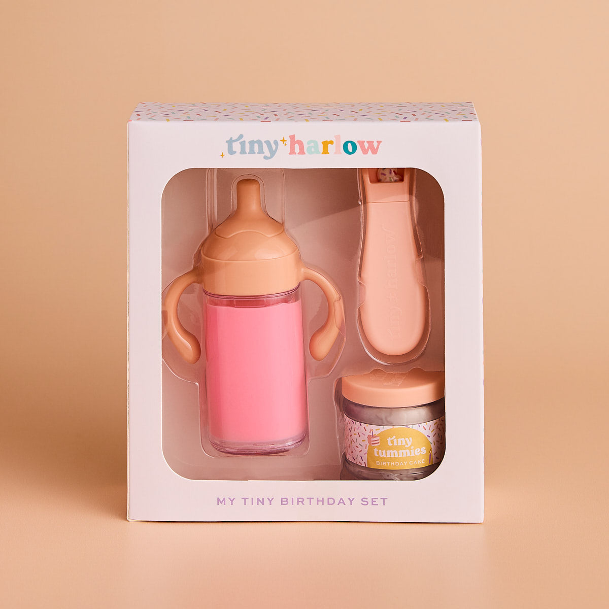 Baby gift set with pink sippy cup, bottle, and jar in a 'tiny harrow' box on a beige background