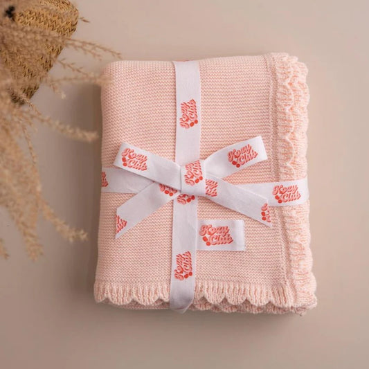 Pink knitted blanket with a white ribbon on a beige background