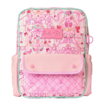 A pink Barbie-themed backpack featuring a whimsical pink pattern, a quilted lower pocket, and a front flap pocket with snap buttons. The Barbie logo is visible on a pink patch on the front.