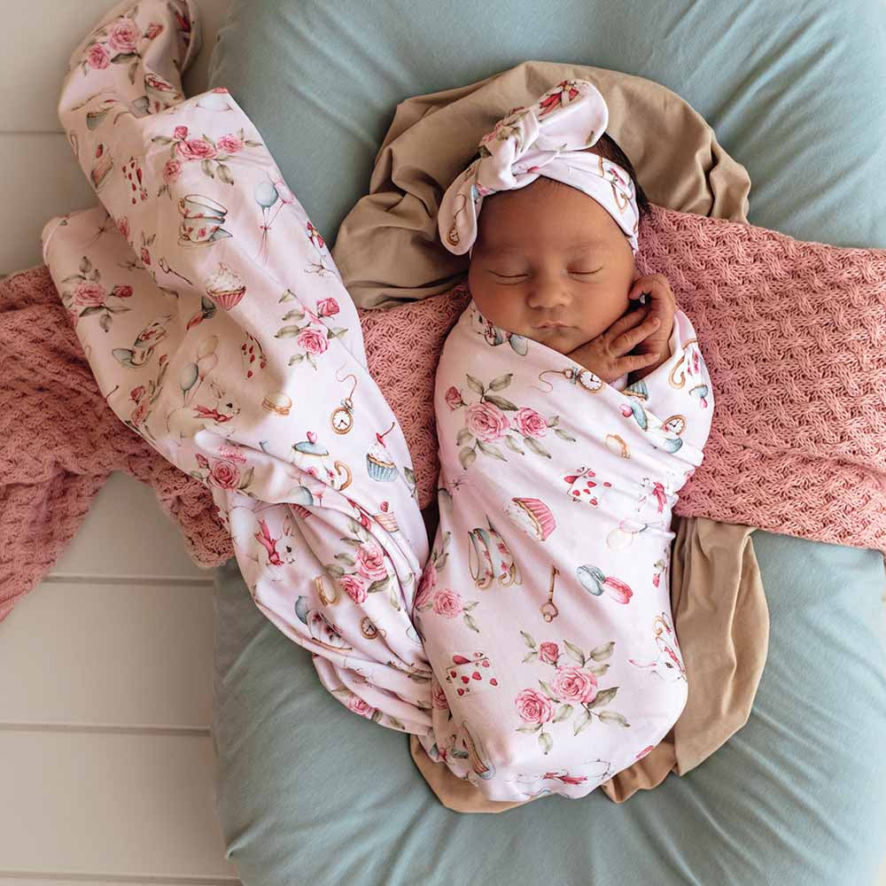 Newborn baby swaddled in a floral blanket with a matching headband on a soft surface.