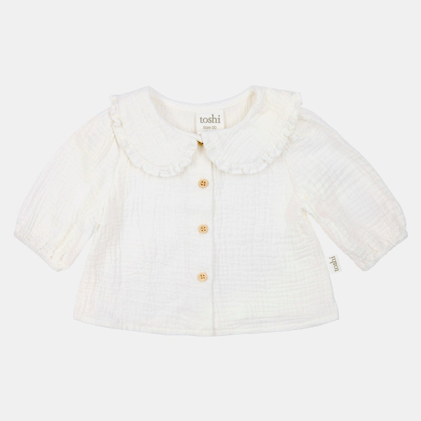 White baby cardigan with ruffled collar on a light beige background