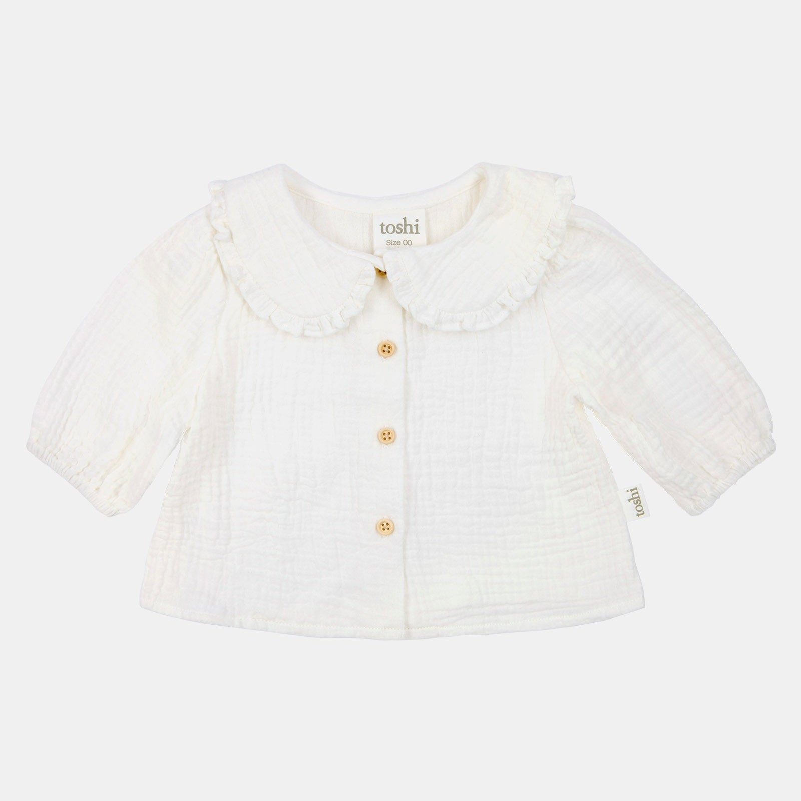 White baby cardigan with ruffled collar on a light beige background