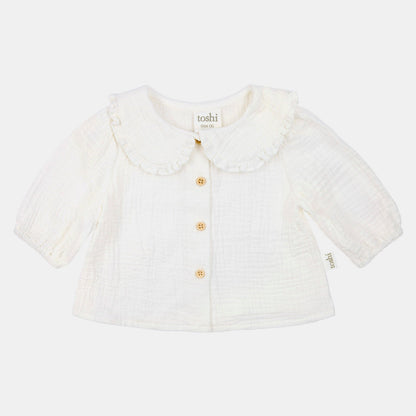 White baby cardigan with ruffled collar on a light beige background