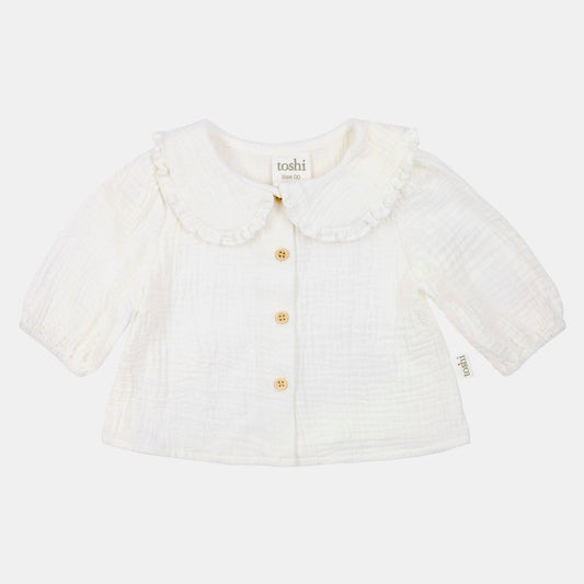 White baby cardigan with ruffled collar on a light beige background