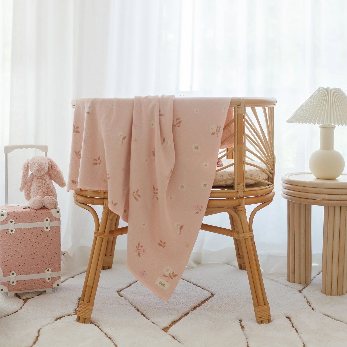 Pink baby blanket draped over a wicker chair in a softly lit room.