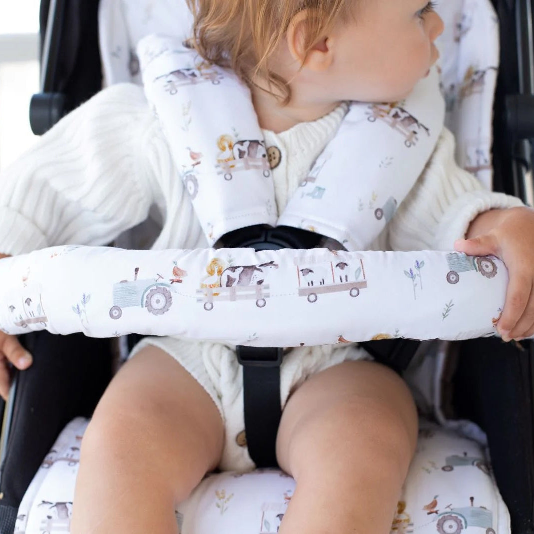 Child holding onto a stroller handle with a patterned cover, sitting in a stroller.
