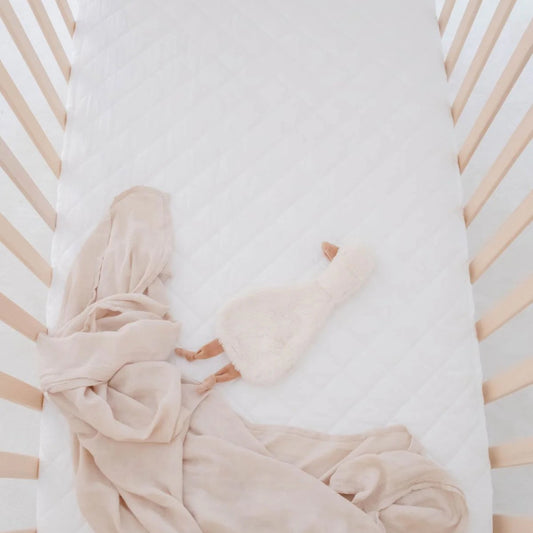 Beige baby blanket and pink plush toy in a crib with white bedding