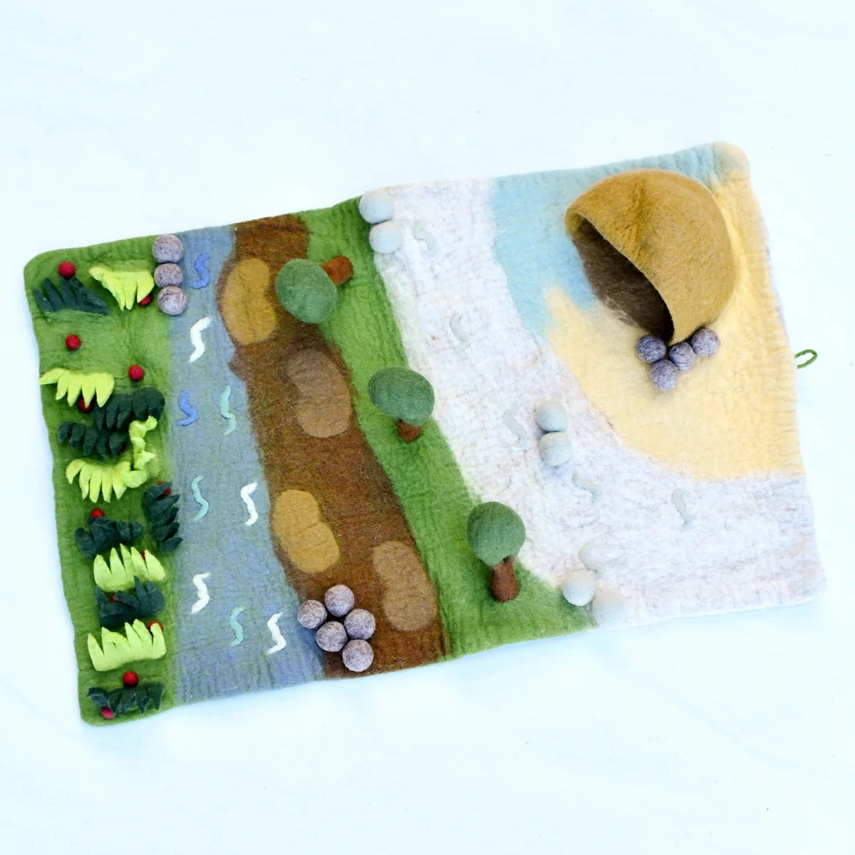A felted wool activity rug depicting a landscape scene with green grass, a brown path, a blue stream, small trees, and a yellow sun, shown on a plain white background.