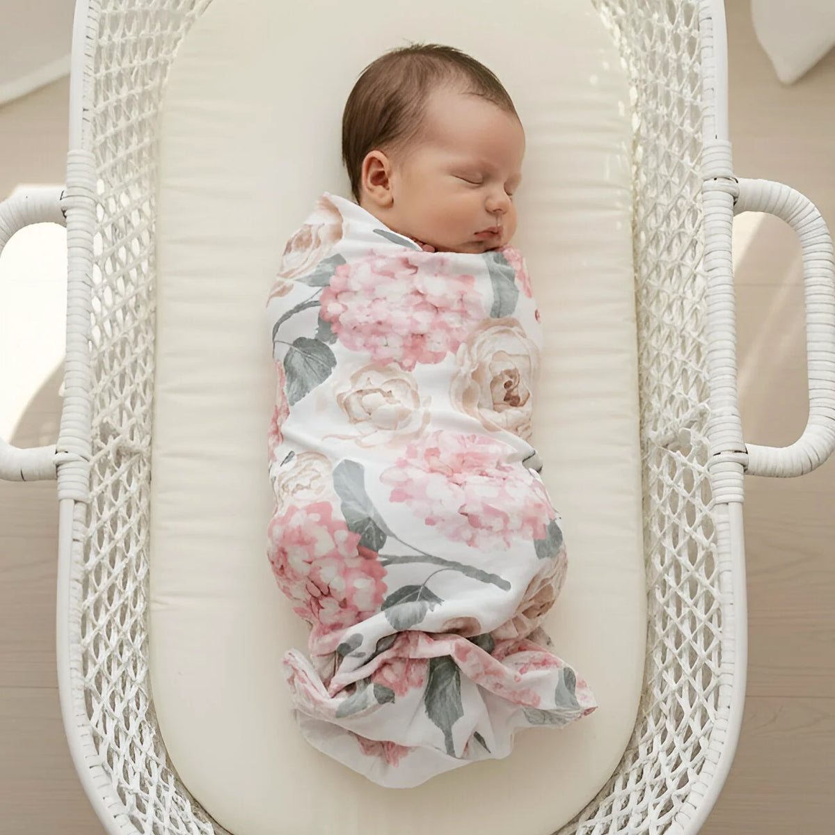 Newborn baby swaddled in a floral blanket in a white crib