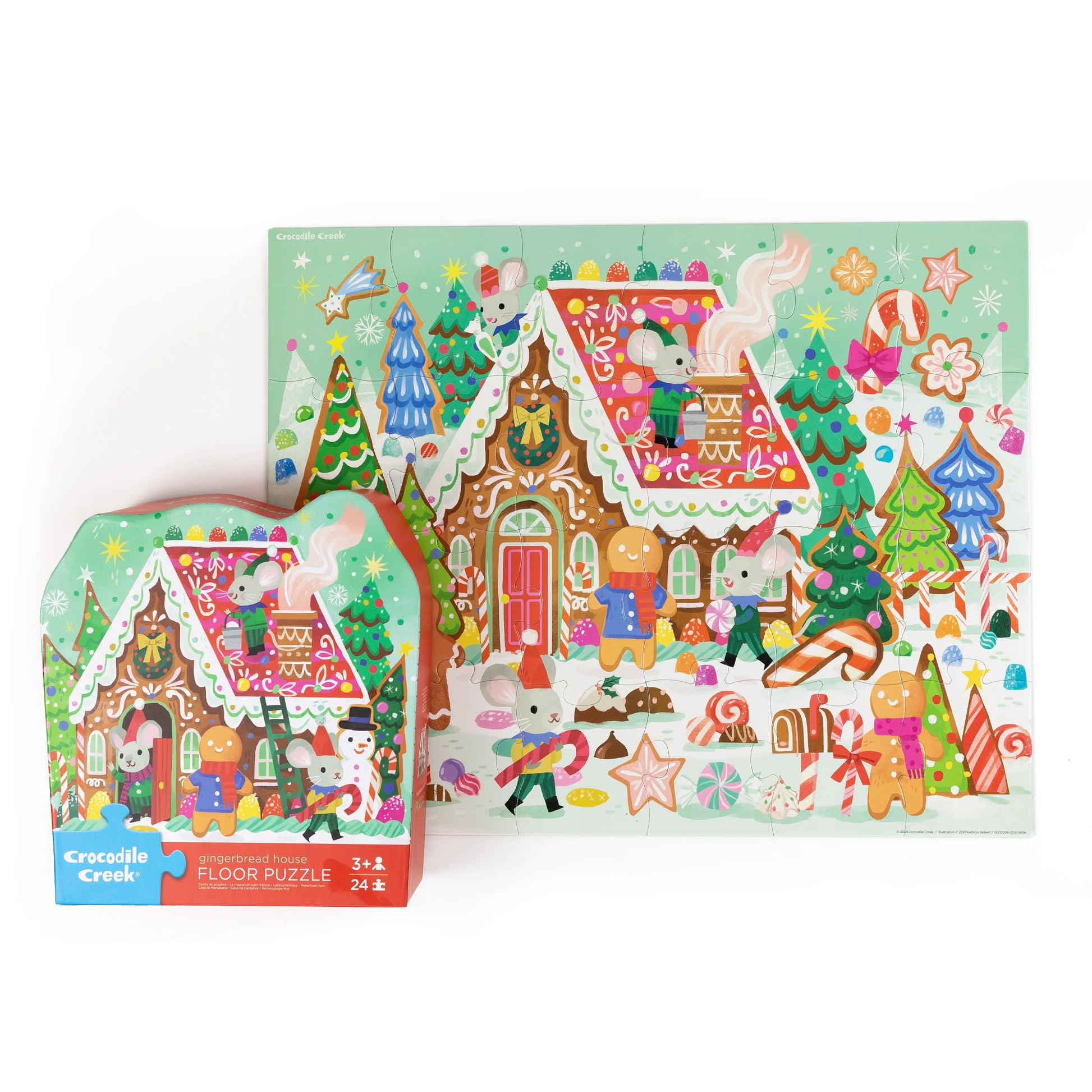 Crocodile Creek Christmas Gingerbread House floor puzzle shown both in its colorful retail box and as the assembled flat puzzle, featuring a festive holiday village scene with gingerbread houses, trees, candy canes, and playful characters.