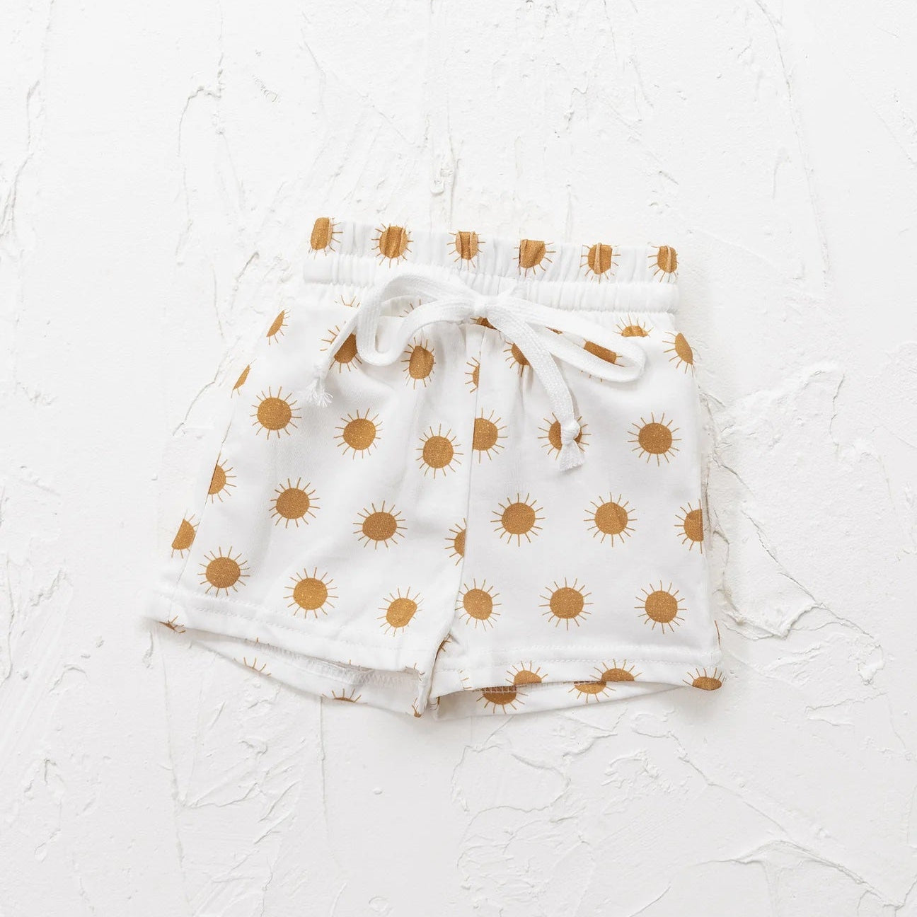 White shorts with gold polka dots on a textured white background