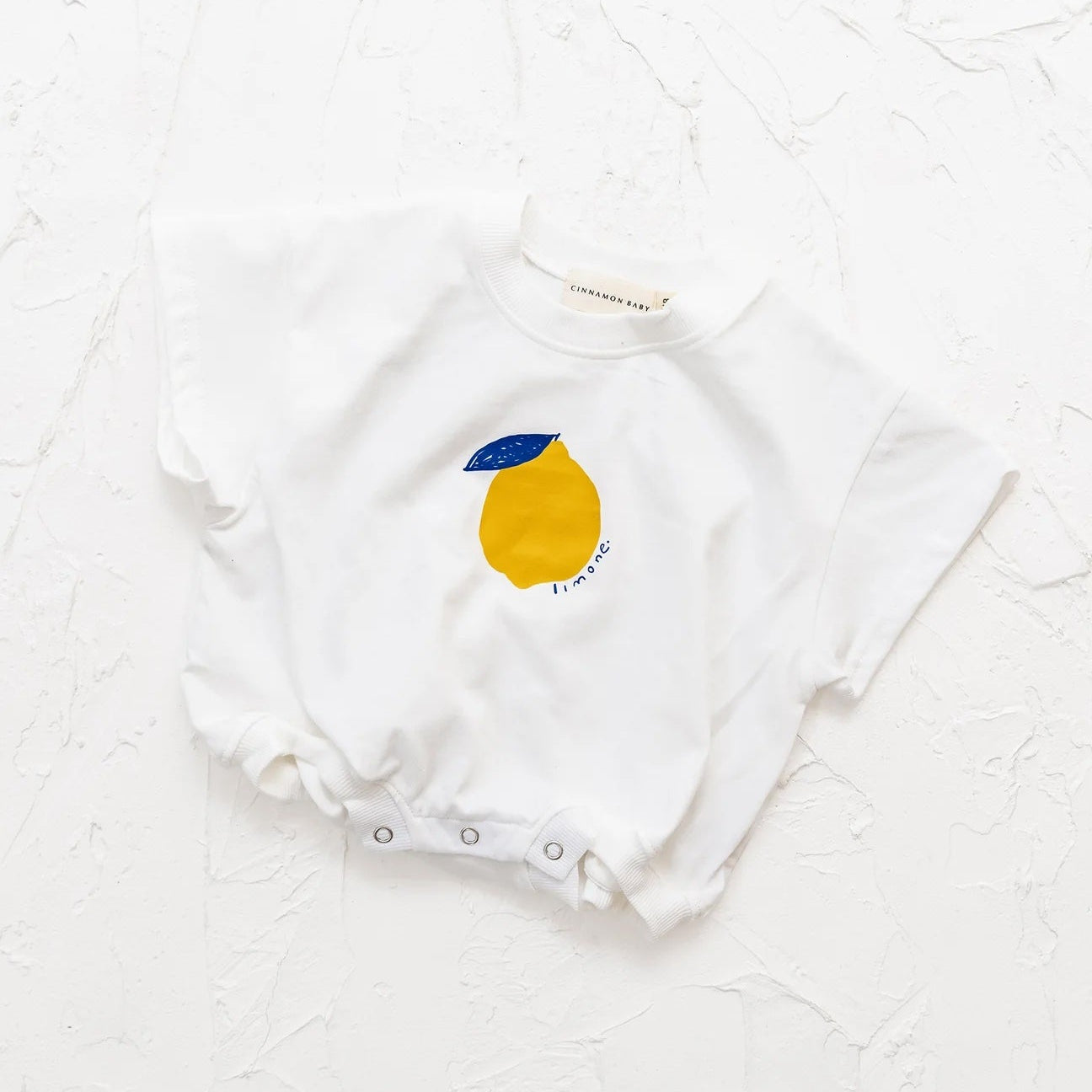 White baby onesie with a lemon design on a white textured background