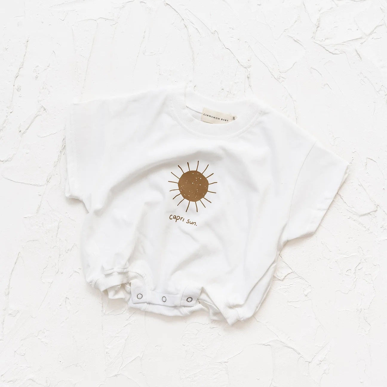 White baby onesie with a sun design on a white textured background